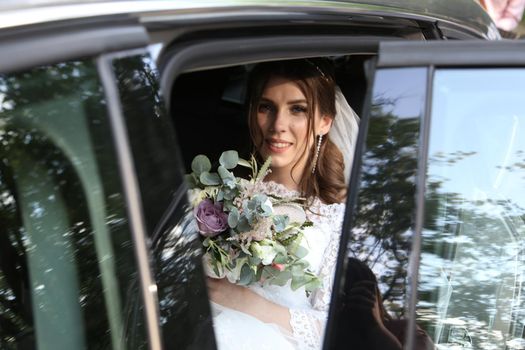 Wedding photo of the bride who is sitting in the car with a bouquet of flowers.