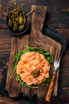 Salmon tartare or tartar with red onion, avocado, arugula and capers. Dark wooden background. Top View