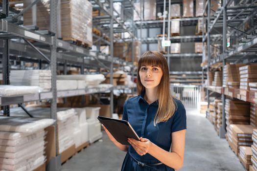Wholesale warehouse. Beautiful young woman worker of store in shopping center. Girl looking for goods with a tablet is checking inventory levels in a warehouse. Logistics concept