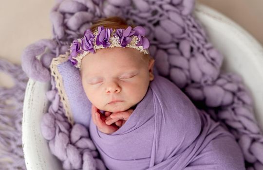 Newborn sleeping wrapped in violet blanket