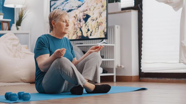 Elder person sitting in lotus position on yoga mat to meditate