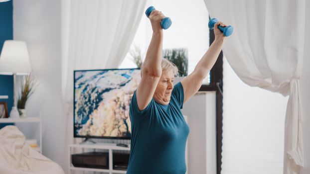 Senior adult training with dumbbells and sitting on toning ball