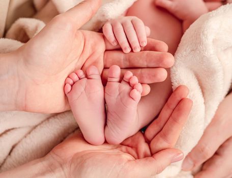 Bare feet of newborn surrounded by family members hands