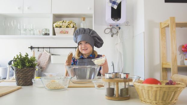 Little girl baker puts batter to the pastry dough for cooking biscuits