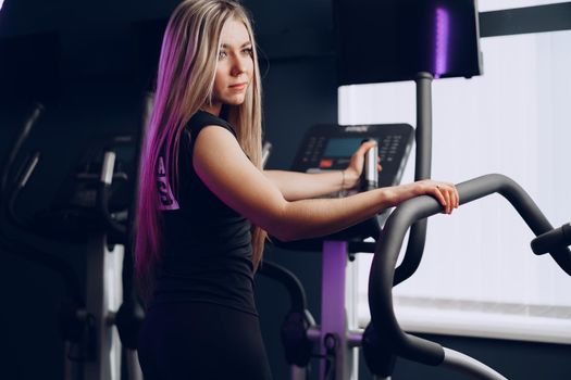 Attractive young blonde woman exercising on cardio training apparatus