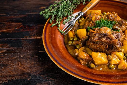 Lamb oxtails ragout with vegetables in a rustic plate. Dark wooden background. Top view. Copy space