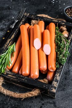 Frankfurter sausages in a wooden tray with herbs. Black background. Top view