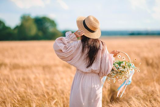 Back view of girl in wheat field. Beautiful woman in dress in a straw hat with ripe wheat in hands