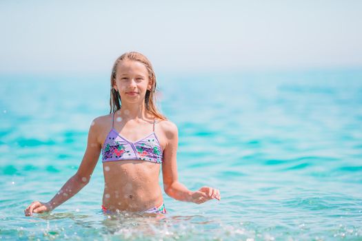 Happy child splashing in the waves during summer vacation on tropical beach. Girl play at the sea.
