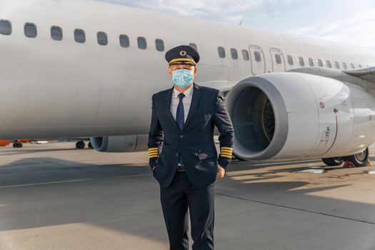 Airline pilot in mask standing near aircraft