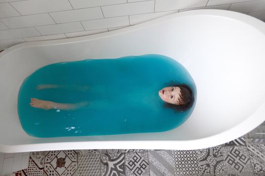 Cute child bathing in blue water in bathtub