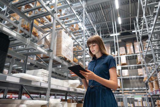 Wholesale warehouse. Beautiful young woman worker of store in shopping center. Girl looking for goods with a tablet is checking inventory levels in a warehouse. Logistics concept