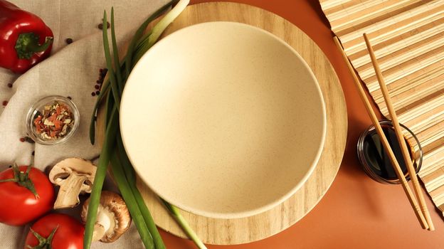 Round wooden board and plate, sauce and various vegetables on the table, wooden stick on a brown background. Flat lay. Copy space in the center of the frame for your text or logo. Recipe and Cooking