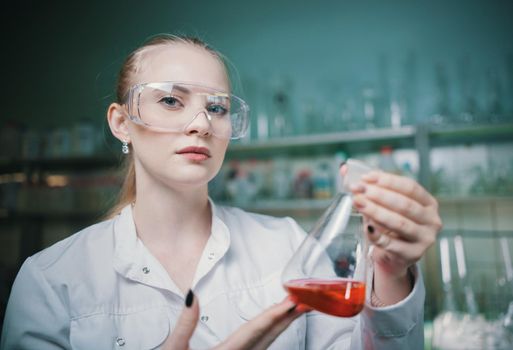 Chemical laboratory. Young blonde woman holding a flask with red liquid in it