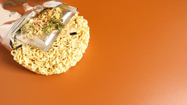 Raw instant food noodles from an unnamed foil packaging without a name close-up with spices and butter. pasta, for the preparation of which it is enough to pour water. Copy space