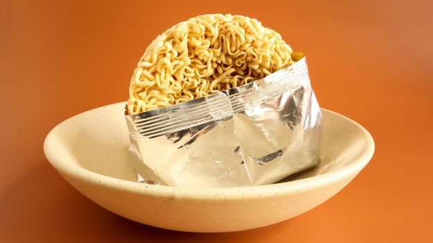 Raw instant noodles in a deep bowl for soup in an open condition from an unnamed foil packaging without a name close-up. pasta, for the preparation of which it is enough to pour boiled water.