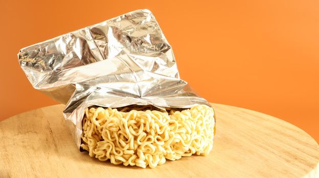 Raw dried instant noodles on a round wooden cutting board in an unnamed foil packaging with no name close up on a yellow background. pasta, for the preparation of which it is enough to pour water