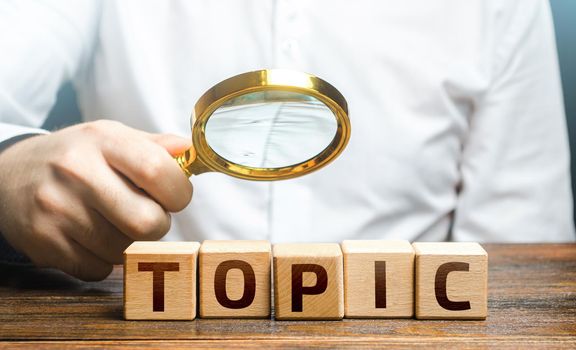 Man examines blocks with topic with a magnifying glass. Conduct research, get an topic explanation. Become an expert, understand the case. Understanding the subject. Assessing value of information