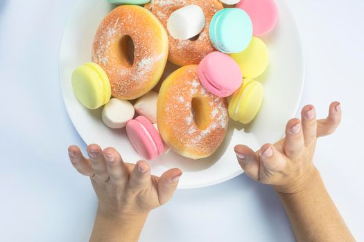 Woman hands making a hand sign of no and refuse for a white plate with fastfood and sugar, top view, healtcare and weightloss concept. donuts, macarons diet