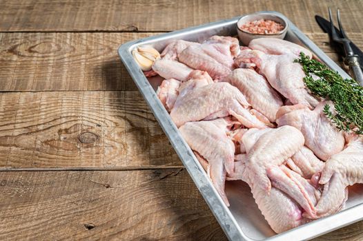 Fresh Raw chicken wings Poultry meat in a kitchen tray with herbs. Wooden background. Top view. Copy space