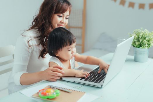 Young mother on maternity leave trying to freelance by the desk with toddler child.