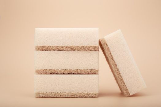 Close up of stack of four beige cleaning or kitchen sponges on bright beige background