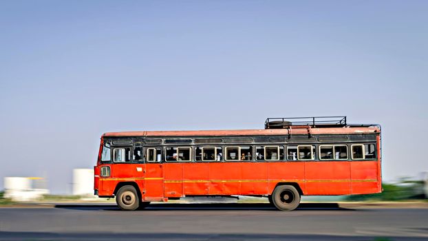 Background blur, pan image of non air-conditioned red intercity bus in Maharashtra, speeding on the street.