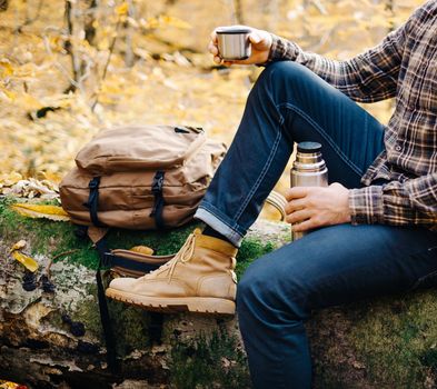 Man resting on fallen tree trunk with thermos.