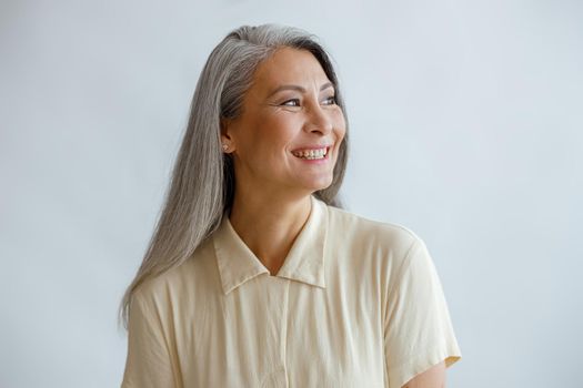 Joyful lmiddle aged lady wearing beige blouse stands on light background