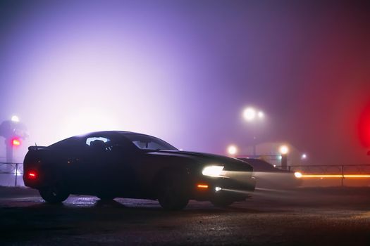 Sport car in the shadows with glowing lights in low light at foggy night, or silhouette of sport car dark background. Selective focus