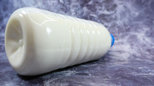 A plastic bottle with a blue cap of fresh regular milk on a dark gray marbled or concrete background. Close-up front view. World milk day concept. Nutrient fluid.