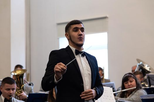 KOROSTEN - NOV, 10, 2019: Young guy orchestra conductor in a black suit. In the background is an orchestra.