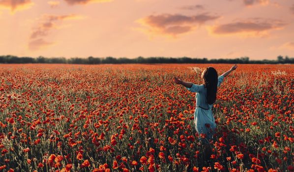 Woman relaxing with raised arms in flower meadow at sunset.