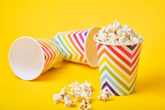 popcorn in a bright festive paper cup on a yellow background, tumbled glasses on a background