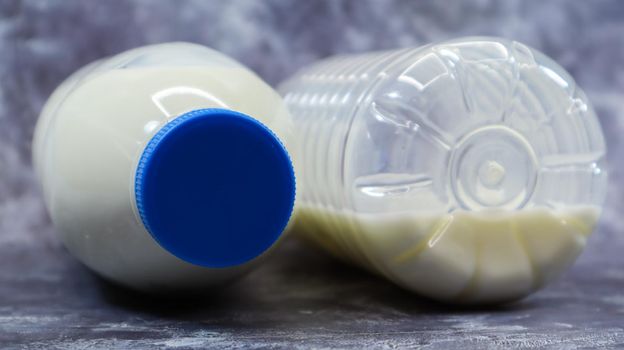 A half-empty and full plastic bottle of fresh regular milk lies on a dark gray marble or concrete backdrop. Close-up front view. World milk day concept. Nutrient fluid.