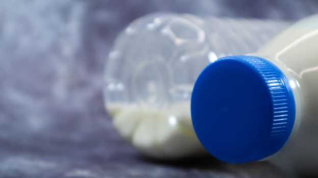 A half-empty and full plastic bottle of fresh regular milk lies on a dark gray marble or concrete backdrop. Close-up front view. World milk day concept. Nutrient fluid. Copy space