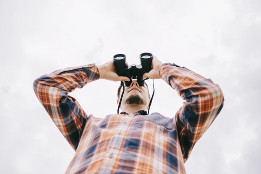 Bottom view of traveler young man watching with binoculars.