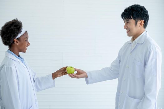 African American young scientist give green apple to her Asian teacher for symbol of respect to the teacher before study in classroom or laboratory.