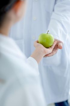 Main focus on green apple that young scientist student give to her teacher for symbol of respect before study in laboratory or classroom.