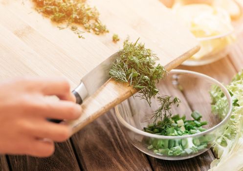 Female hands putting sliced greenery into a plate.