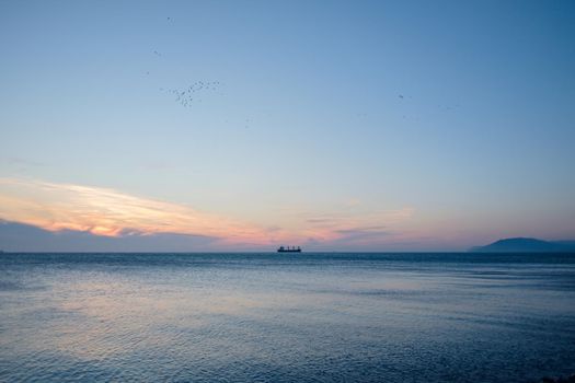 Ship sailing at horizon in sea at sunset.