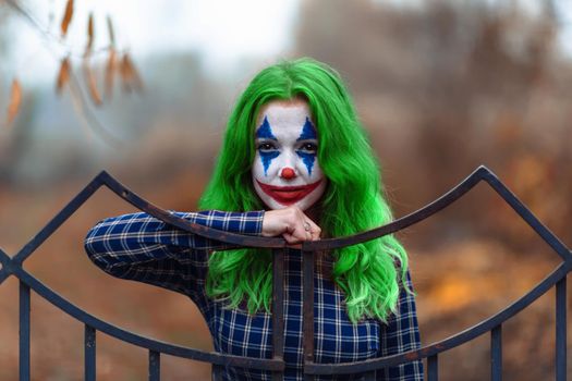 Close-up portrait of a greenhaired woman in chekered dress with joker makeup on a blurry background.