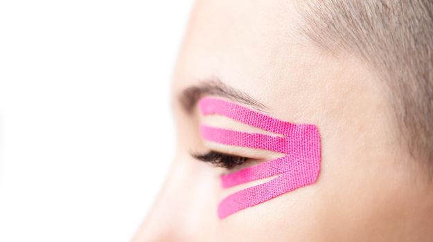 Anti-aging kinesiology tape on female eyelid, close-up.