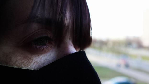 Close-up side view of a young woman in a protective mask. Caucasian girl with green eyes taking security measures against the coronavirus pandemic against the background of an empty city. Covid-19