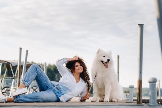 a happy woman with a big white dog lies on a pier near the sea at sunset