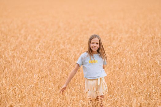 Adorable preschooler girl walking happily in wheat field on warm and sunny summer day