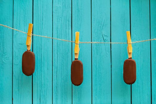 three delicious chocolate ice creams on rope near turquoise background. summer food concept
