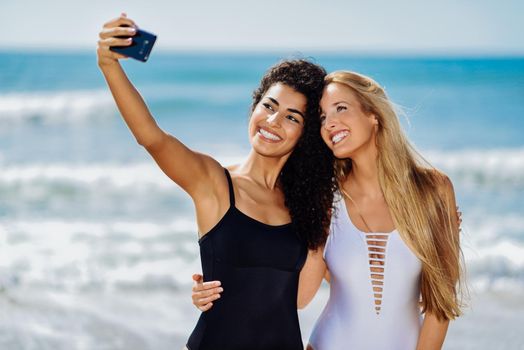 Two women taking selfie photograph with smartphone in the beach