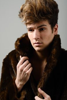 Attractive young man wearing fur coat with modern hairstyle
