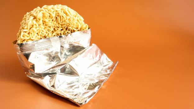 Raw dried instant noodles in open condition from an unnamed foil packaging without a name close-up on a yellow background. pasta, for the preparation of which it is enough to pour water